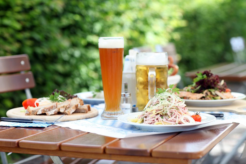 Gartentisch gedeckt mit einem Teller Wurstsalat, Glas Hefeweizen